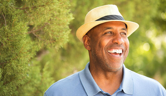 man in blue polo and fedora smiling amongst trees