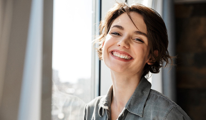 Woman with dental implants in San Antonio, TX smiling by window