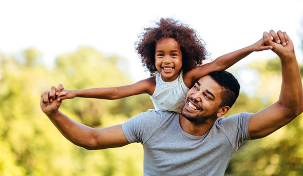 A father and daughter playing together outside and smiling 