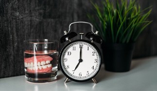 Dentures in glass of water next to clock