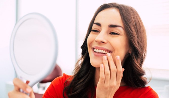 a patient admiring her new smile after receiving dental implants in San Antonio, TX