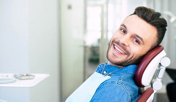 Man smiling in a dental chair with denim jacket