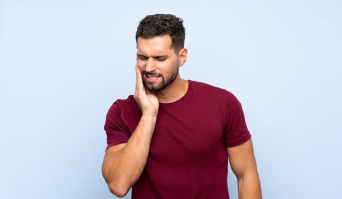 Man in burgundy t-shirt experiencing mouth pain