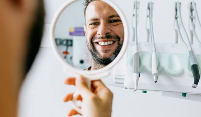 Happy dental patient’s face reflected in hand mirror
