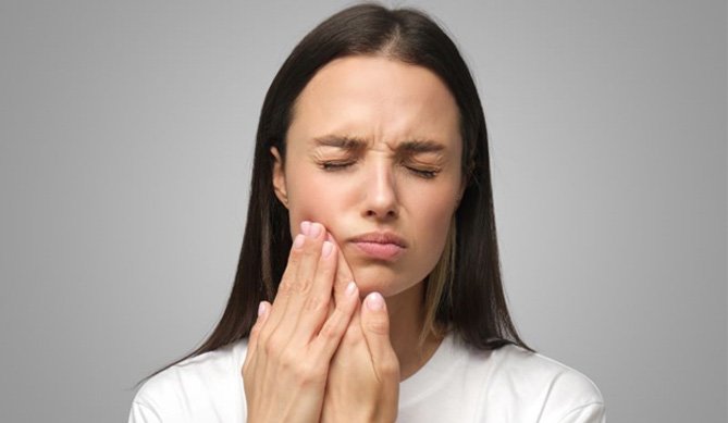 Woman touching her cheek, wearing pained expression