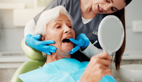 Dentist in blue gloves gently touching woman’s teeth and neck